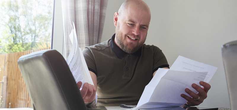 Smiling adult reviews paperwork at table.