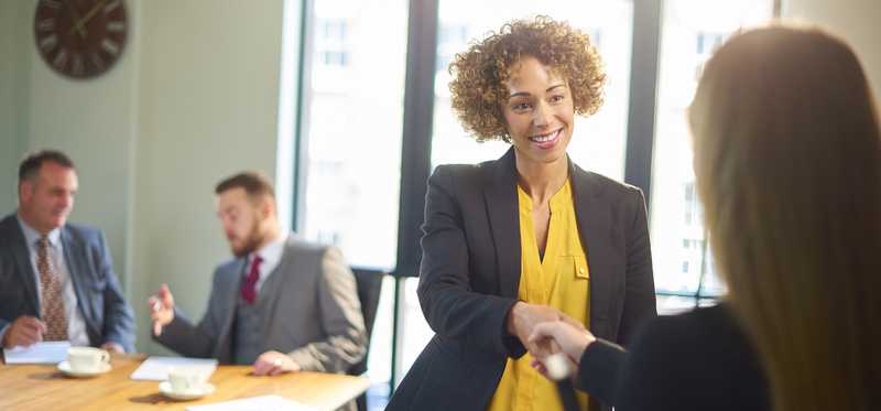Two adults shake hands in a conference room.