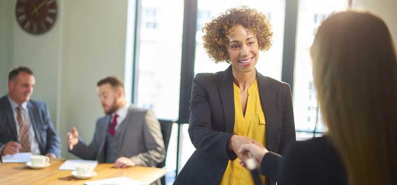 Two people standing and shaking hands in office meeting setting.