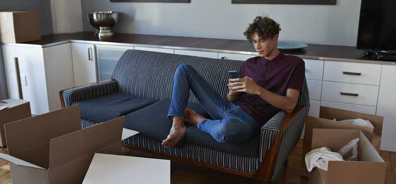 Person sitting on couch surrounded by moving boxes.
