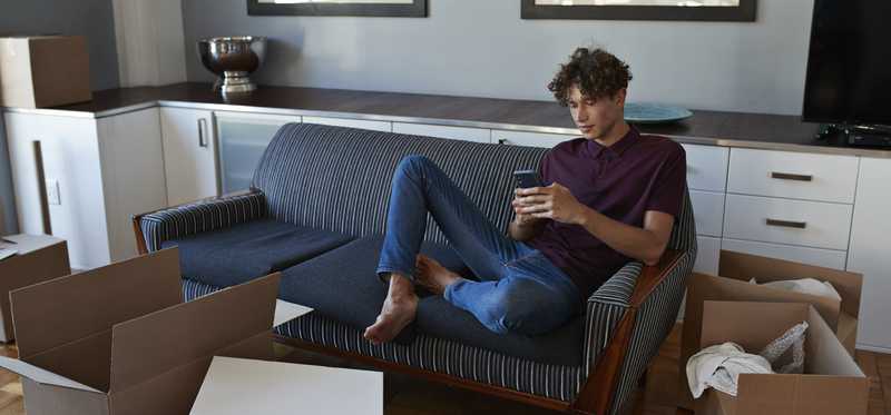 Person sits on couch in apartment with unpacked boxes.