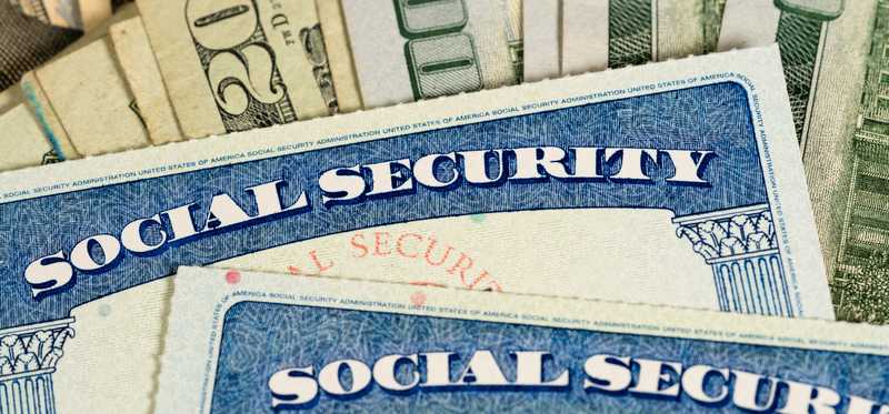 Two social security cards sit atop a pile of various valued dollar bills.