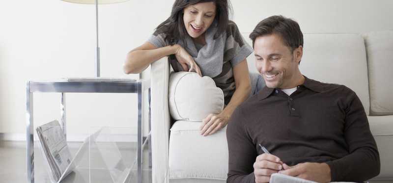 Two people smile while looking at laptop screen in living room.