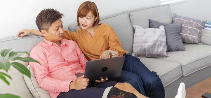 Two people relaxing on couch and discussing something on laptop.