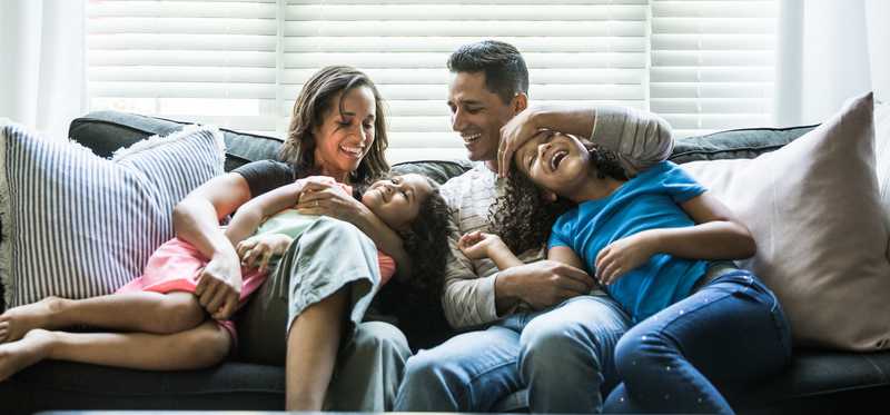 Happy adults and children snuggle on couch.