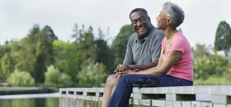 Two people sitting on dock by lake.