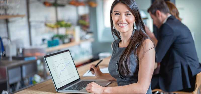 Person standing at bar in restaurant while working on laptop.