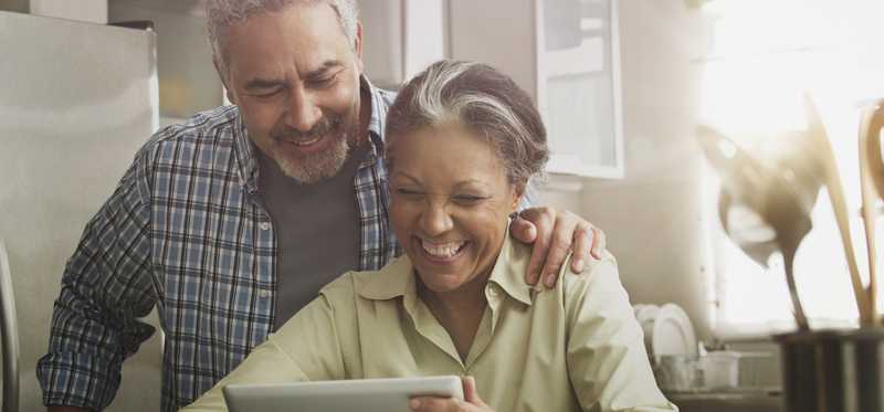 Two people smiling at tablet at home.