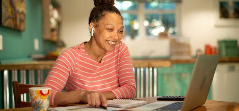 Smiling person looking at laptop at kitchen table.