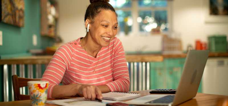Smiling person looking at laptop at kitchen table.