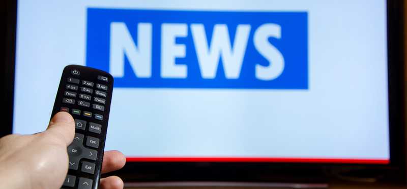 Person holding remote watching TV news.