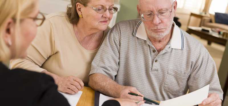 An elderly couple looks at paperwork and talks with an advisor.