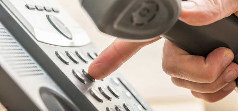 A finger dialing numbers on a phone.