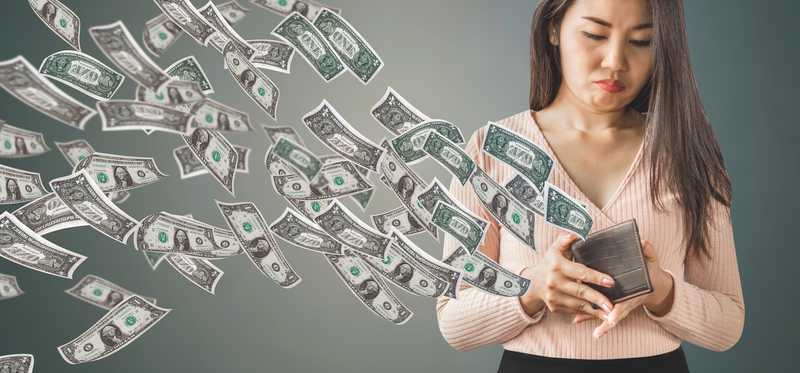 Person unhappily holding an open wallet, as lots of dollar bills fly out of it.
