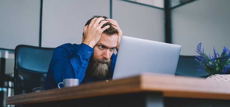 Person holding head and appearing upset while looking at computer screen.