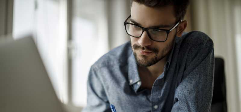 Person in glasses taking notes from laptop.