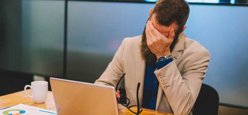Person sitting at desk looking upset with hand covering face.