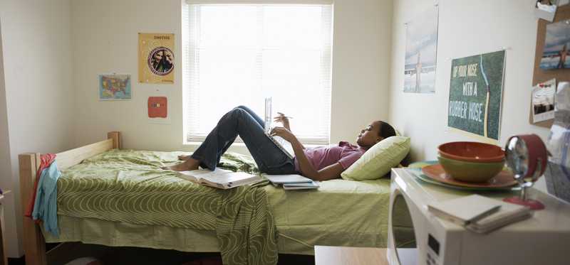 Person lying on a bed in a dorm or apartment bedroom.