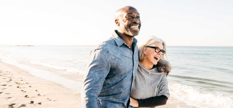 Two happy people walking with arms around each other on beach.