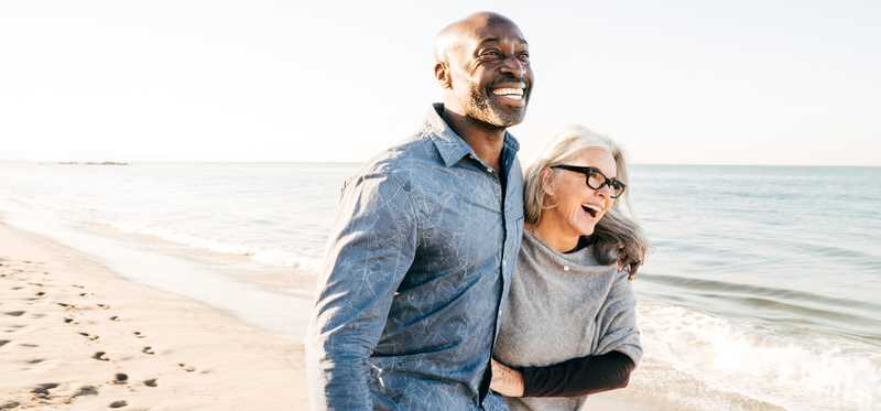 Two individuals smile and laugh while walking together on beach.