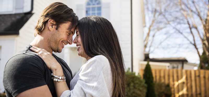 Two happy people hug in front of house.
