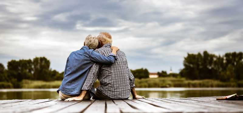 Couple cuddling while sitting by water on dock
