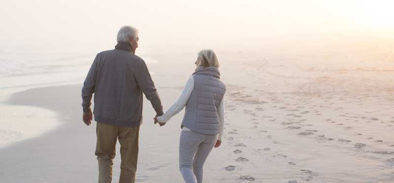 Couple holding hands and walking on beach.