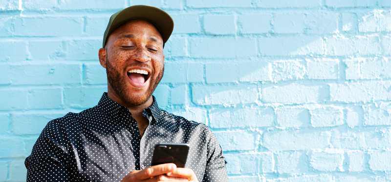 Happy person holding phone and standing near blue wall.
