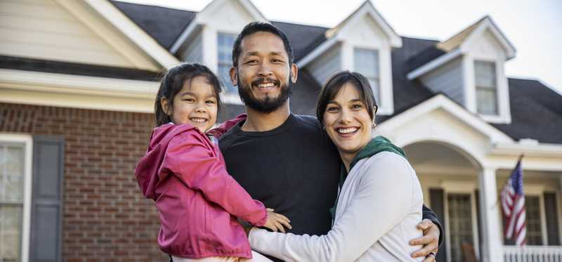 A smiling family standing in front of a house.