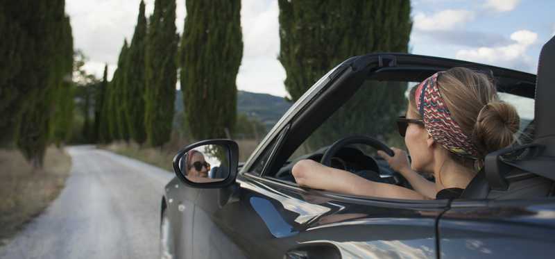 Woman driving convertible on road lined with trees
