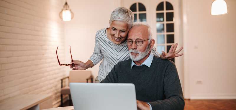 Two people happily review information on laptop screen at home.