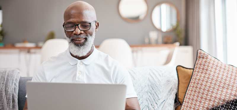 Person sitting on couch at home while looking at laptop and smiling.