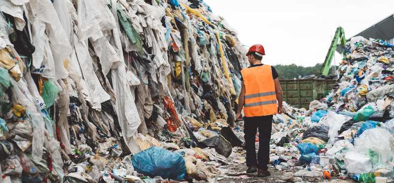 A person walking through large piles of trash at a landfill.