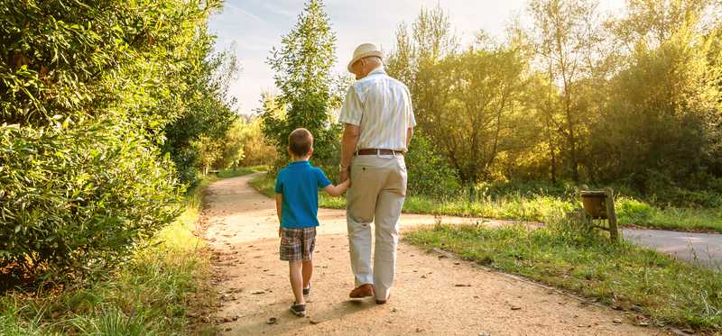 Older man walks outside with young child.