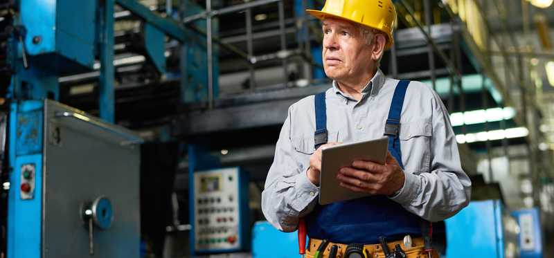 A senior man in a construction outfit and hard hat.