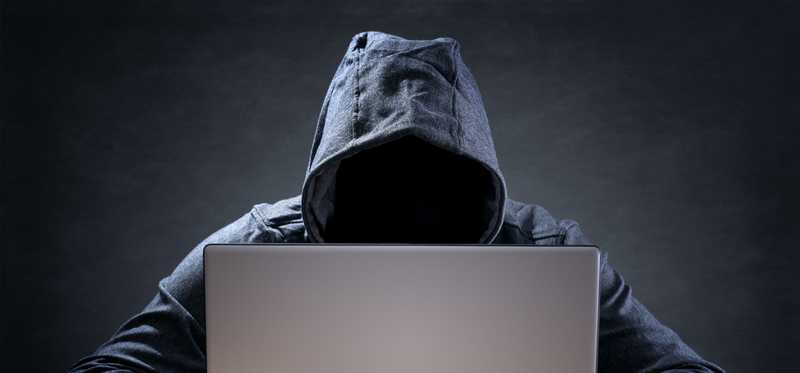 Faceless hacker in hoodie at laptop