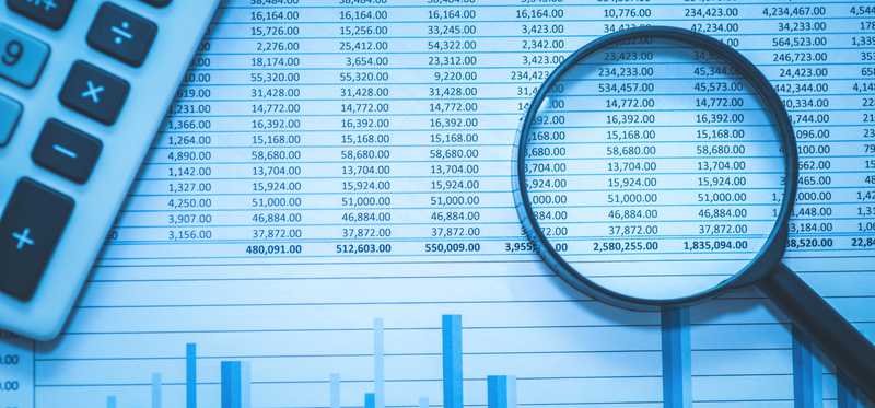 A magnifying glass over a sheet of numbers and data.