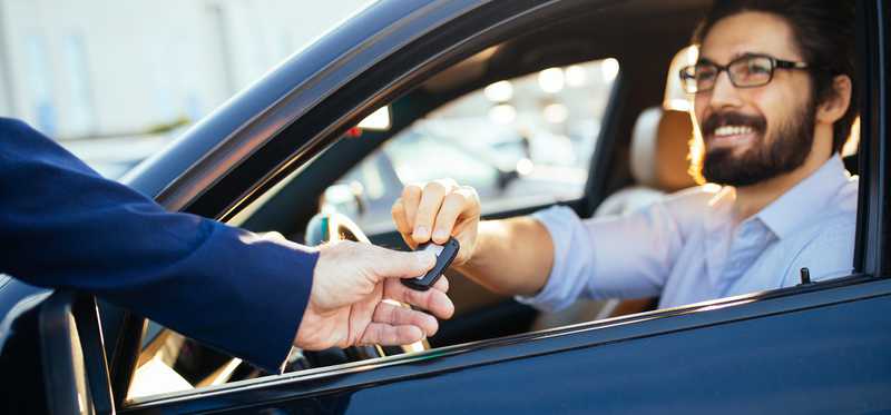 Person hands car keys to man sitting inside a car.