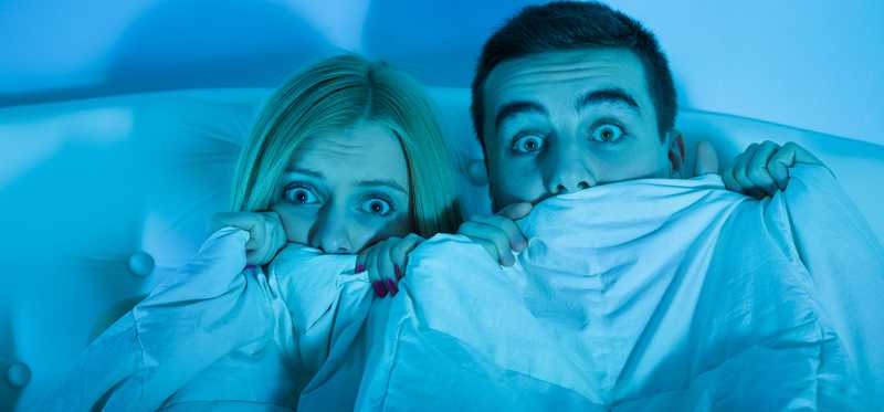 A young couple holds a blanket over their faces in fear.