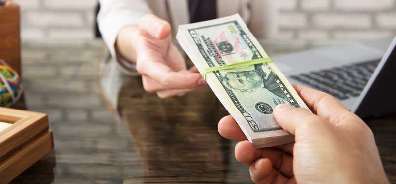 Woman being handed a bundled stack of cash.