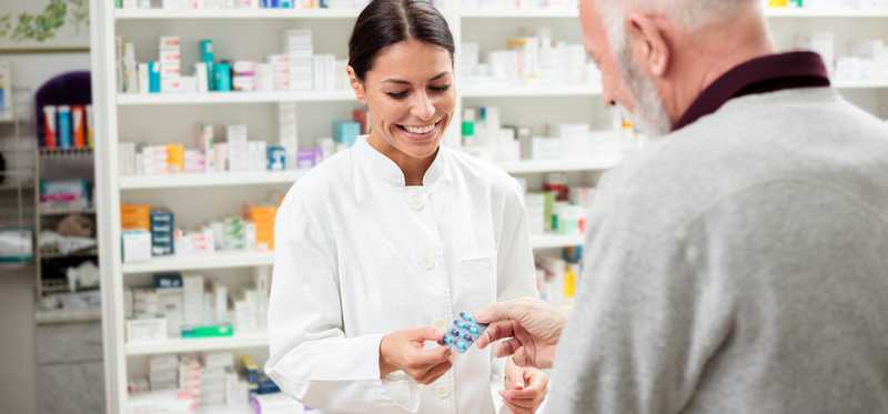 Pharmacist handing medication to an older male.