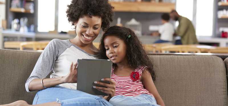 Mother and daughter using a tablet on the couch.