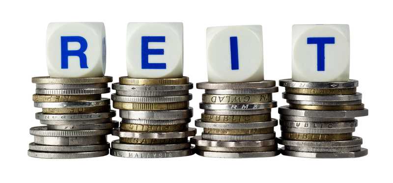 Word REIT spelled out on dice sitting atop coins from all over the world.