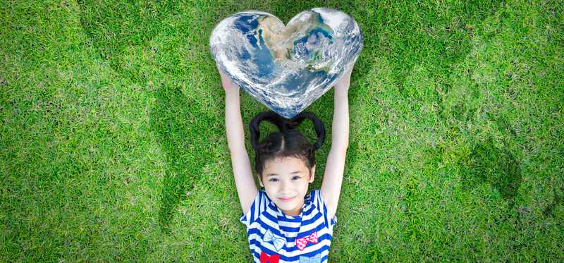 Girl holding heart shaped world while laying on grass with a map of the world