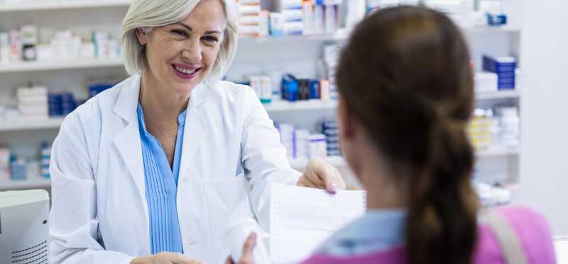 a smiling female pharmacist handing a paper to a customer