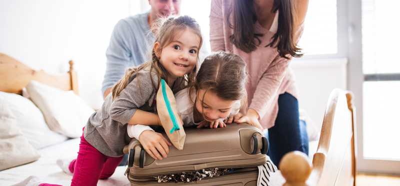 A family working together to close a full suitcase in a room.