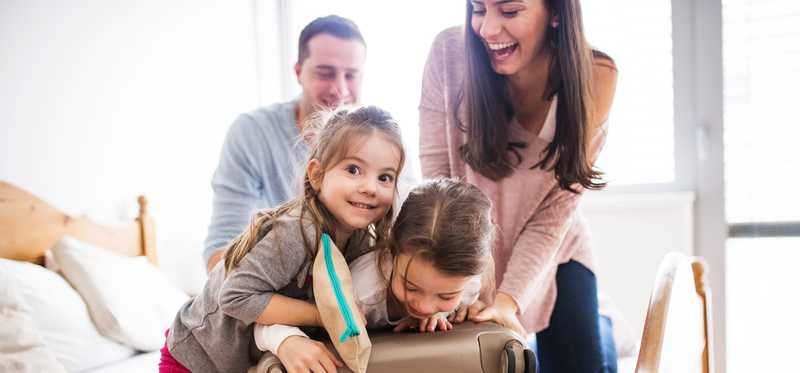 A family working together to close a full suitcase in a room.
