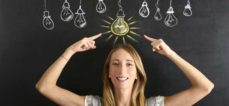 A woman pointing to a lit chalk lightbulb above her head.