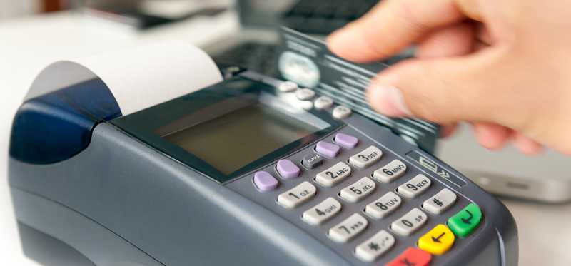 A hand swiping a credit card through a credit card machine