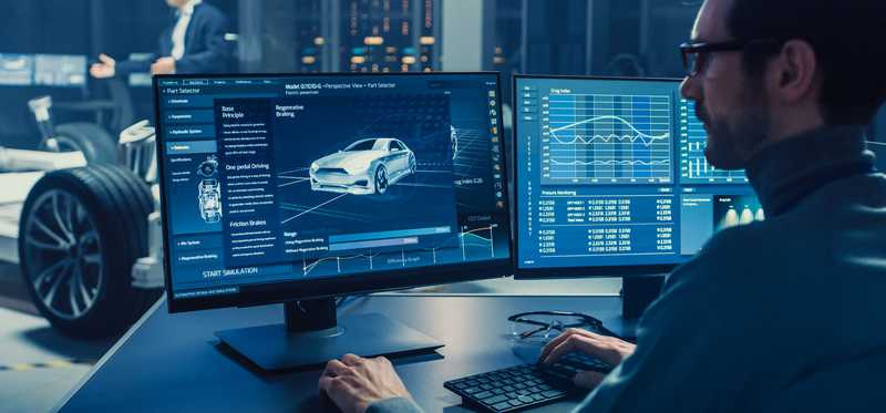 A man working at a computer with a simulation of a car on the screen.